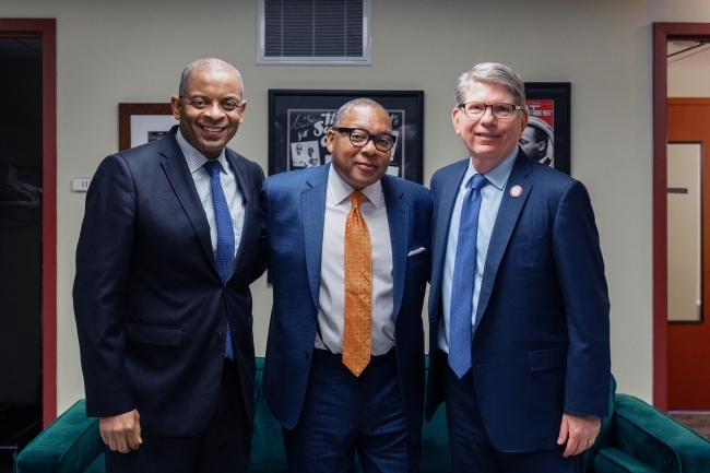 three older men in suits stand together smiling