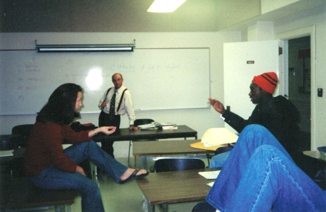 two young people debate in a classroom with an older man professor looking on