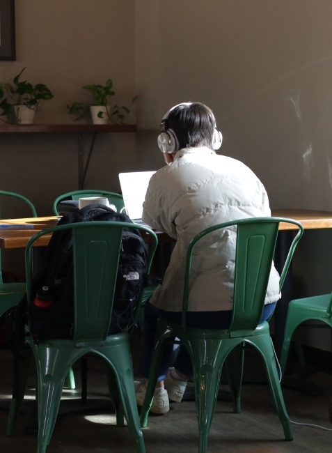 a young person wears headphones while typing on laptop in a coffee shop