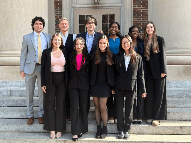 a group of young people in business formal clothing standing together in front of an academic building