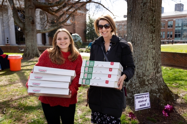 two women hold boxes of donuts while smiling outside on a sunny day