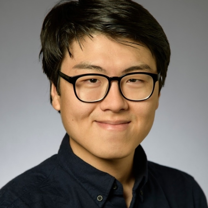 a young Asian male wearing a black shirt and glasses smiling