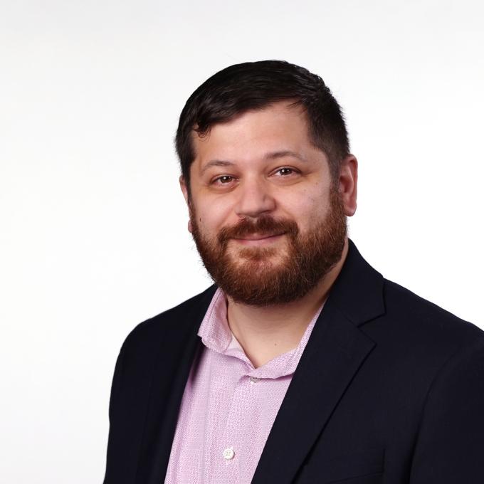 a middle aged white man wearing a pink collar and black blazer