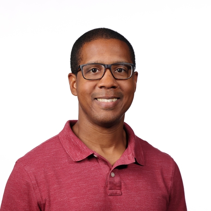 a middle aged Black man wearing glasses and a red collared top