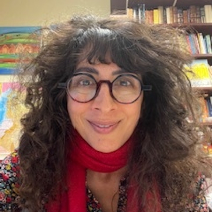 a middle aged white woman with curly brown hair wearing glasses and a red scarf