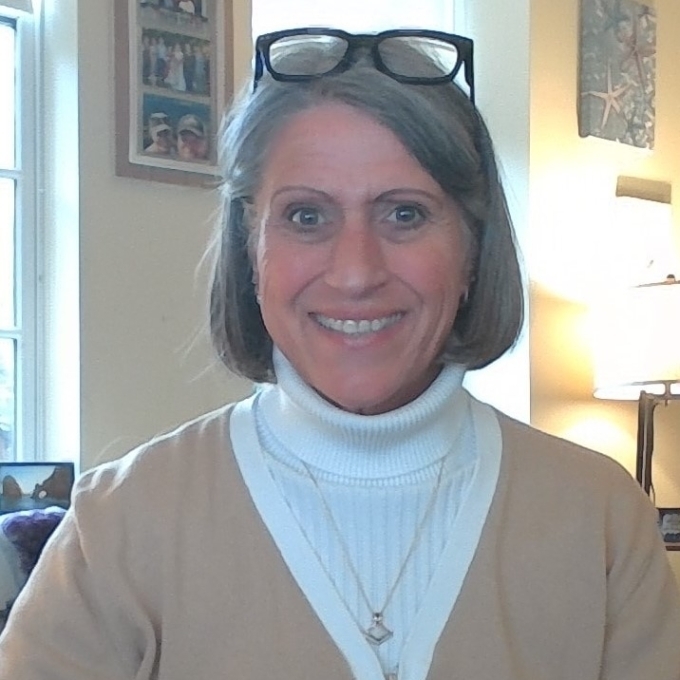 a white woman with grey hair wearing a white turtleneck and black glasses