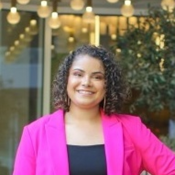 a young woman wearing a pink blazer with curly dark hair