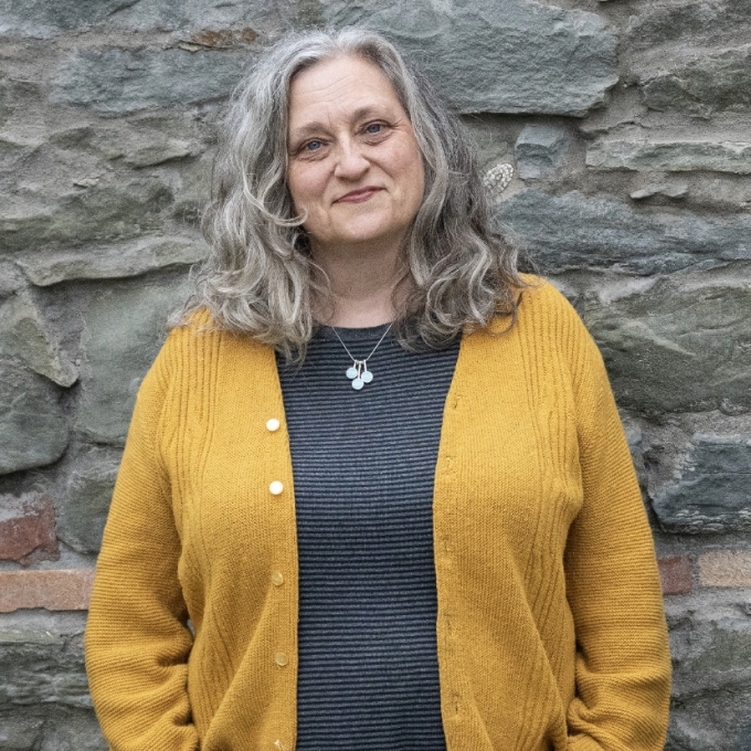 a white woman with grey hair wearing a grey shirt with a yellow sweater