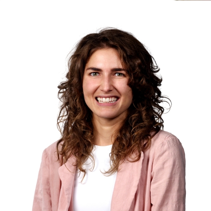 a young woman with curly brown hair wearing a pink blazer