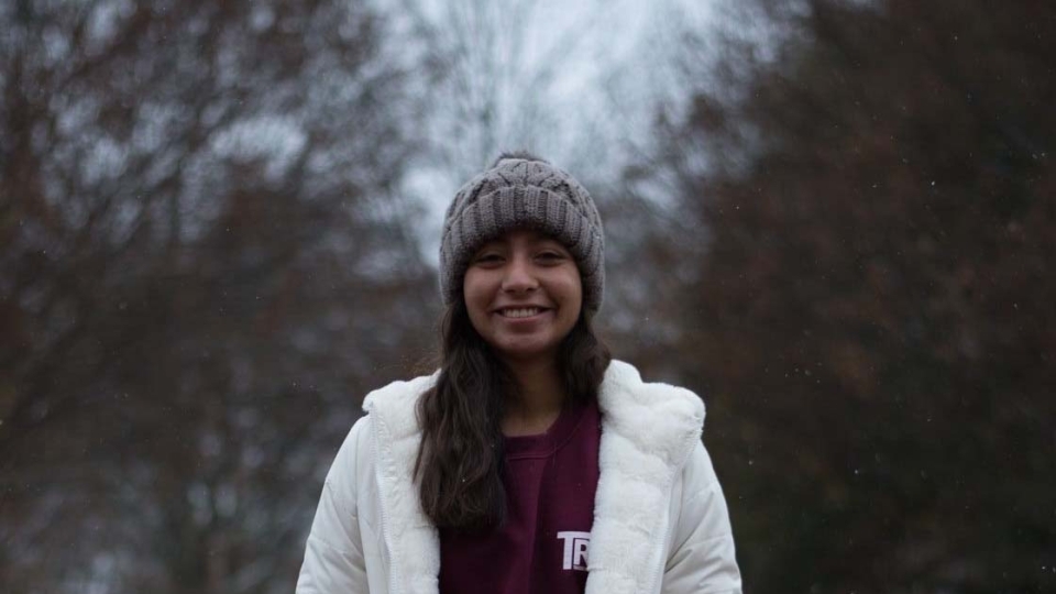 Yara poses in winter clothing in front of trees