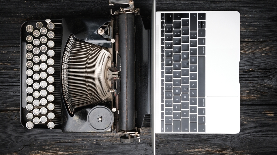 Antique typewriter next to modern laptop on wooden table