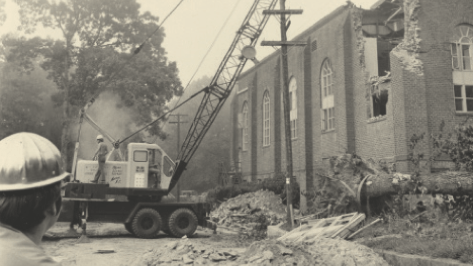 black and white photo of construction machine tearing down walls of former Johnston Gymnasium