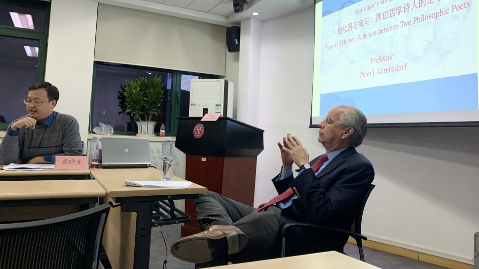 Professor lecturing at a table with powerpoint behind him