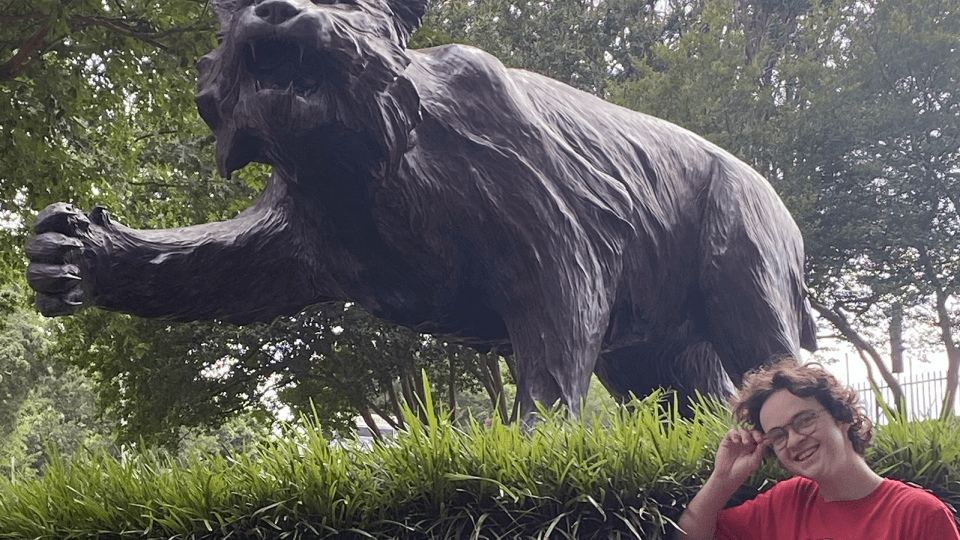 a young student wears a Davidson t-shirt while smiling and standing in front of a wildcat statue