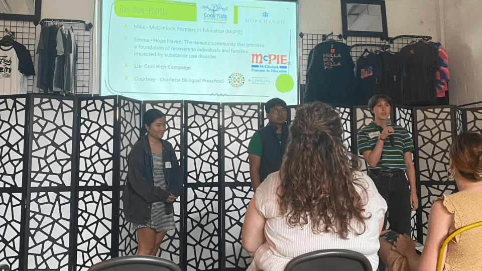 three young people present in front of a screen in a large room of people