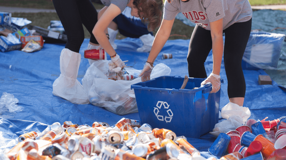 two young people holding recycling bins while sorting through piles of trash