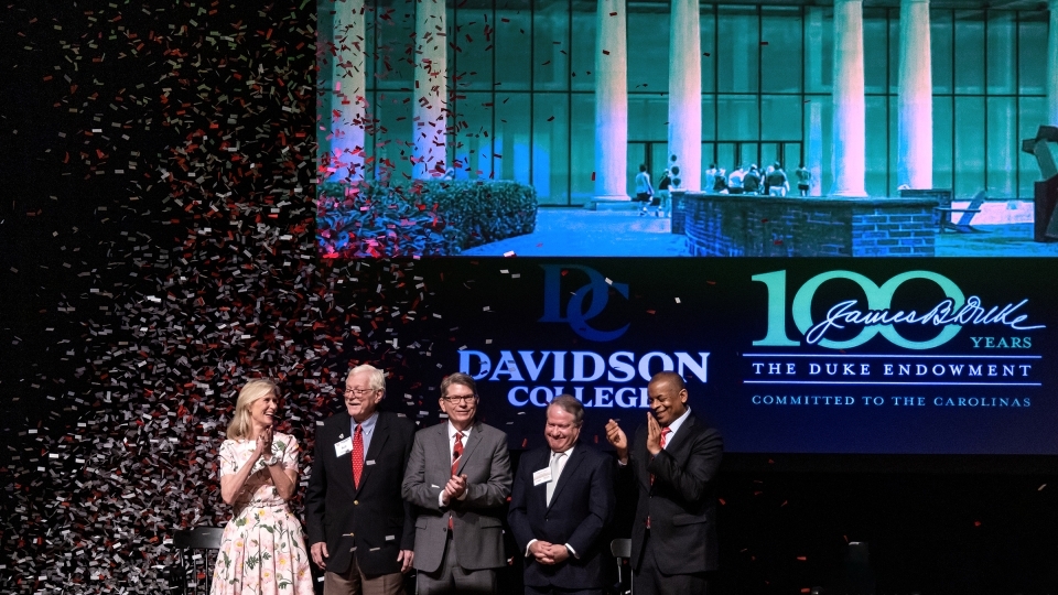 a group of five people standing on a stage clapping as confetti falls around them