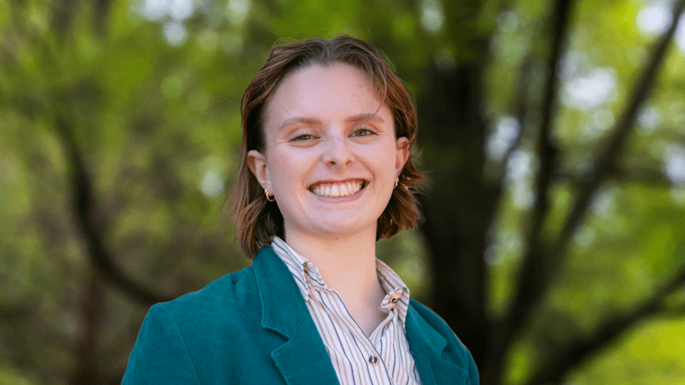 a young white woman wearing a collared shirt and jacket smiles