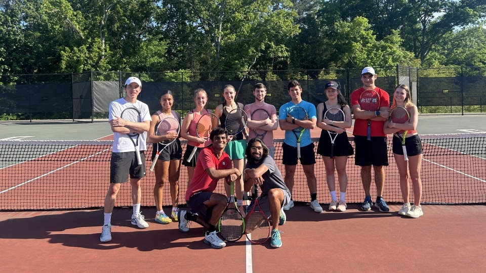 a group of students with tennis rackets on a court smiling