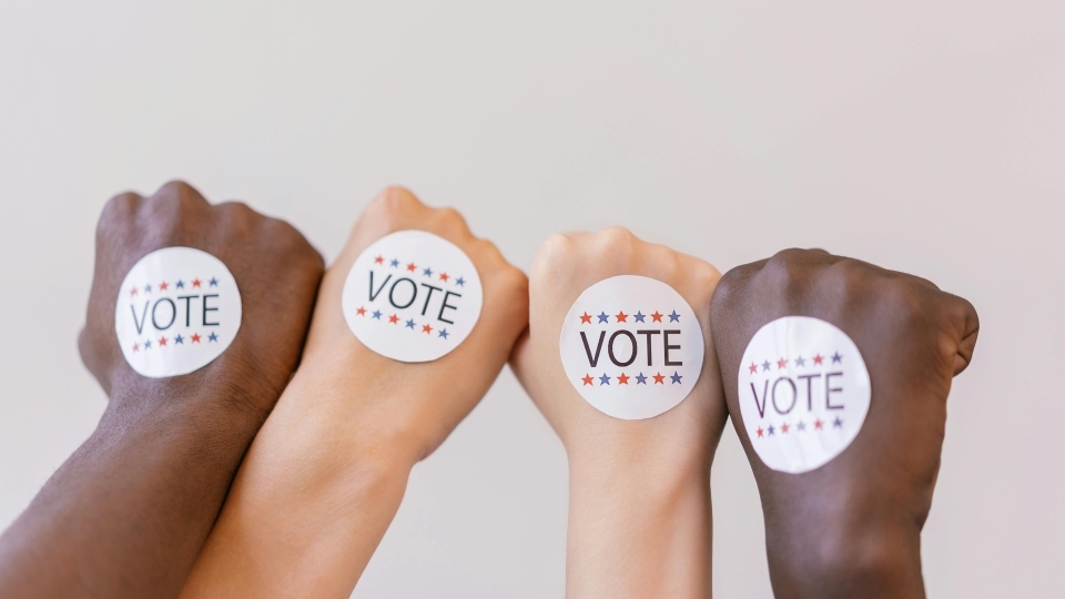 four hands in fists with "vote" stickers