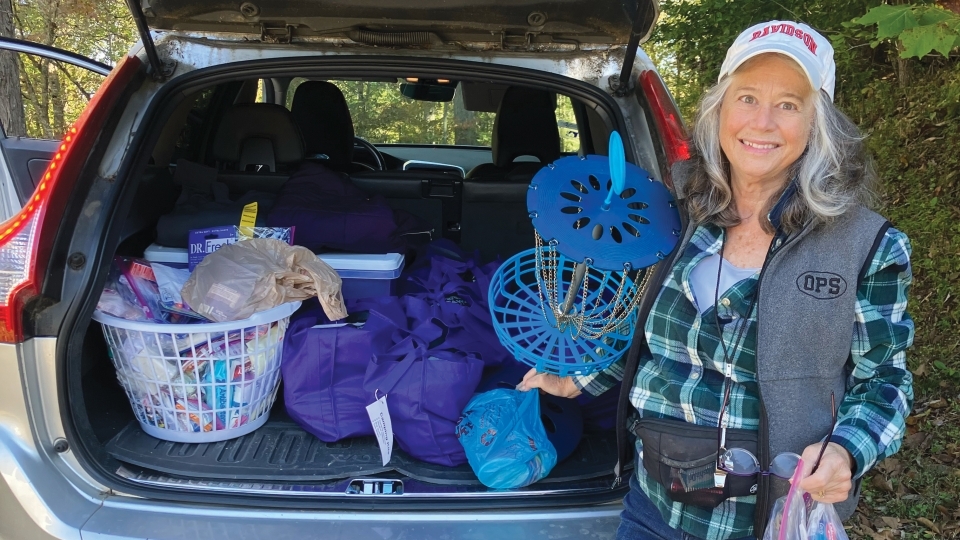 a woman poses in front of a car trunk filled with supplies for hurricane relief