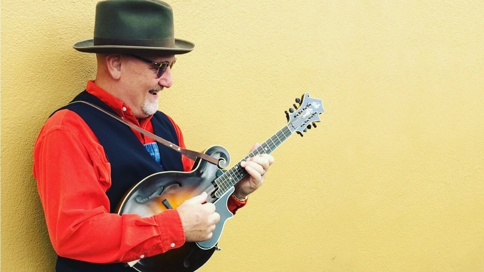 Mike Compton playing the mandolin against a yellow wall