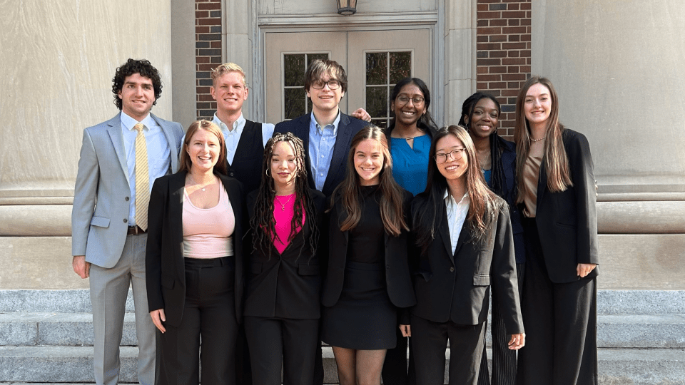 a group of young people in business formal clothing standing together in front of an academic building