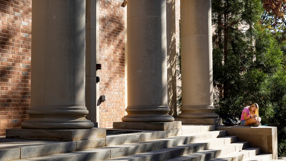 a student sits on the steps of an academic building reading a book