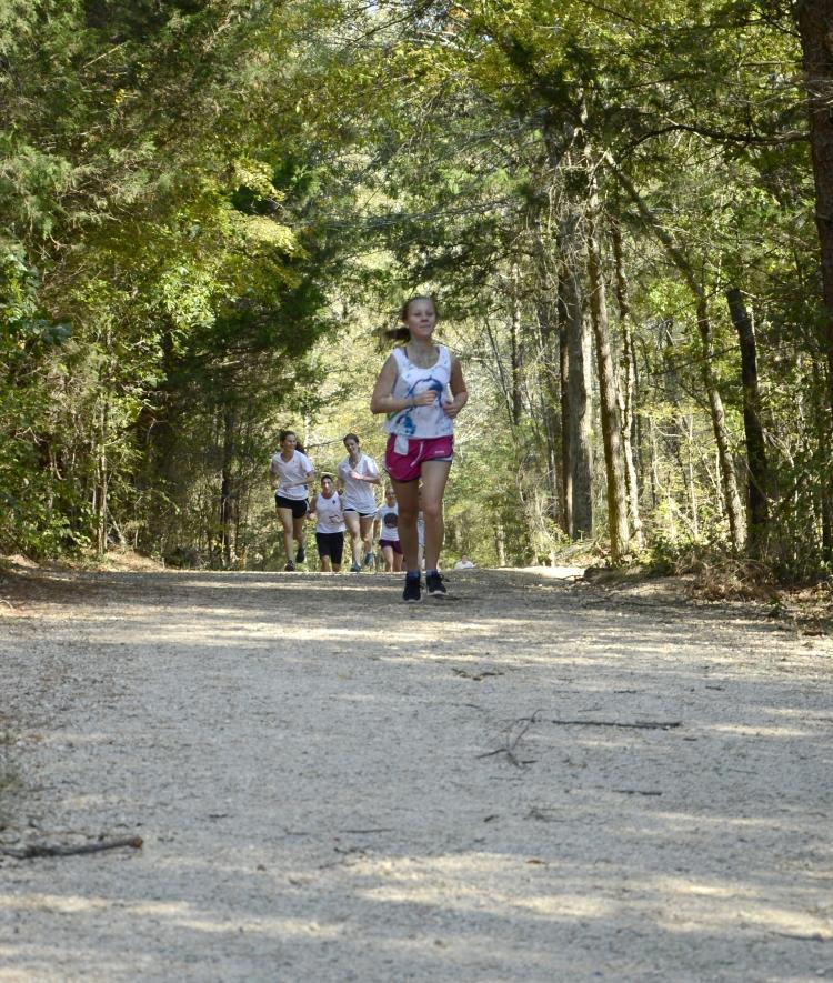 a young woman runs on a cross country trail in the woods