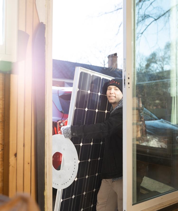 Student carrying solar panel through sliding glass door