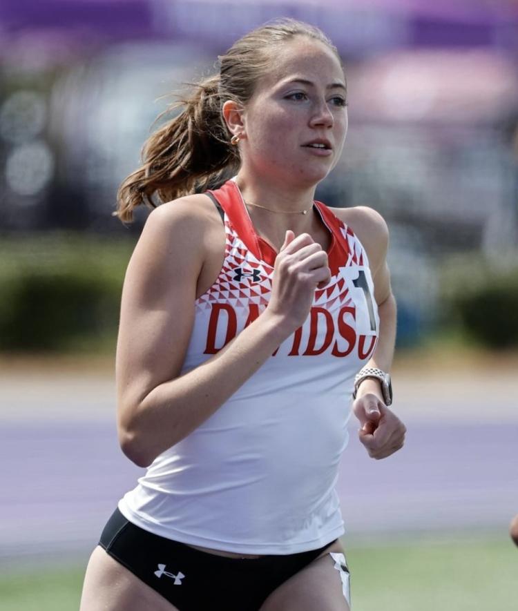 a young white woman wearing a "Davidson College" uniform runs on a track