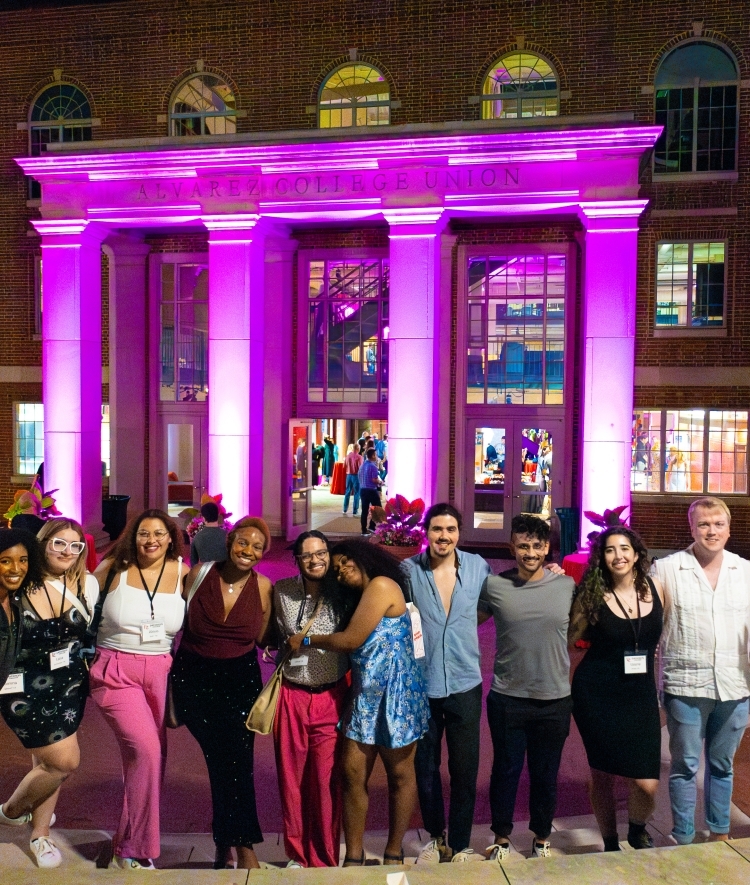 Young alums with arms around each other in front of a purple illuminated union