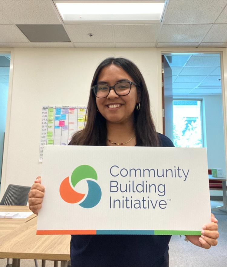 a young woman holds a sign that says "community building initiative"