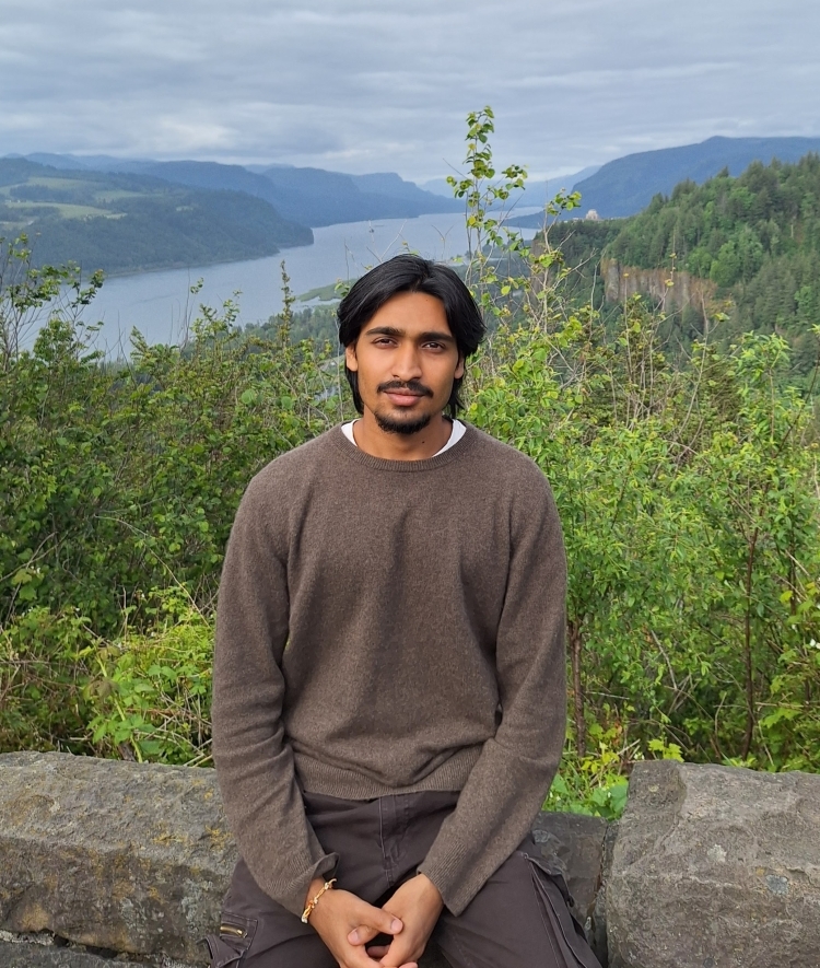 a young man sits on a stone wall overlooking a river