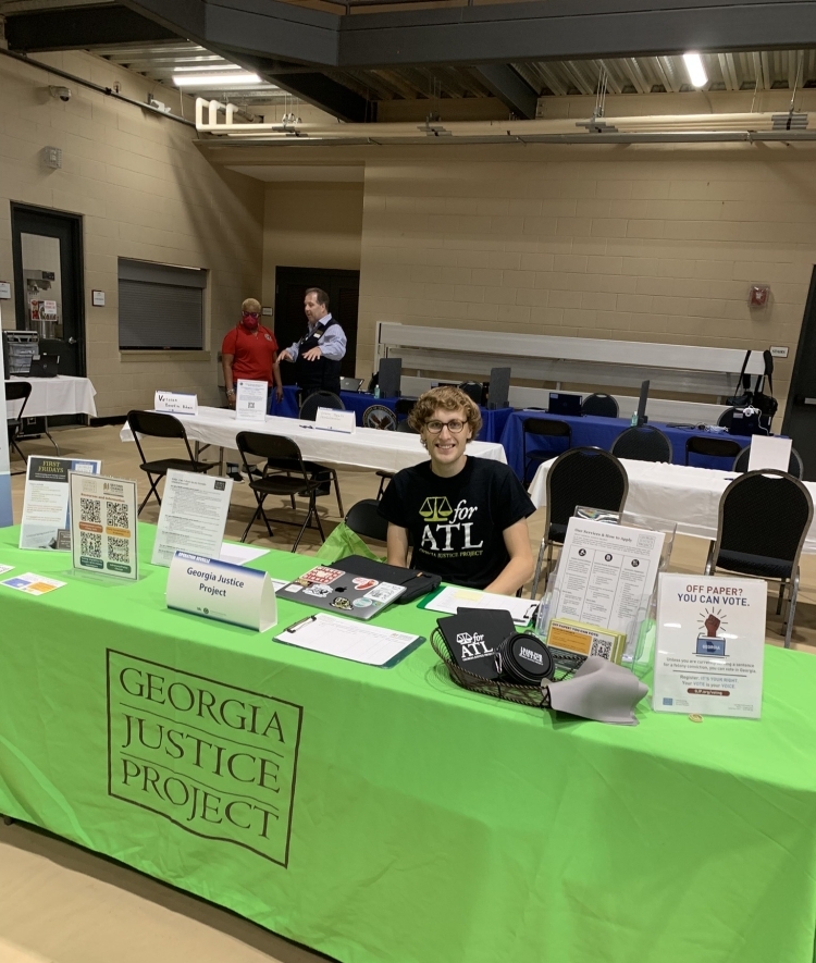 a young white man sits at a table that reads "Georgia Justice Project"