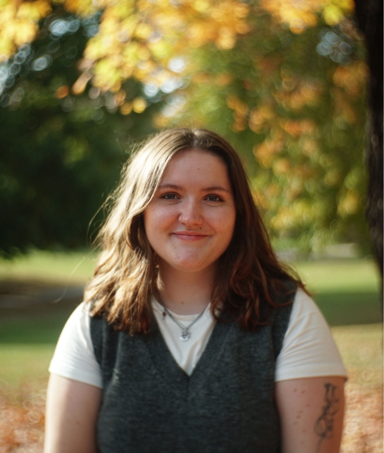 a young white woman wearing a tshirt and sweater vest outside