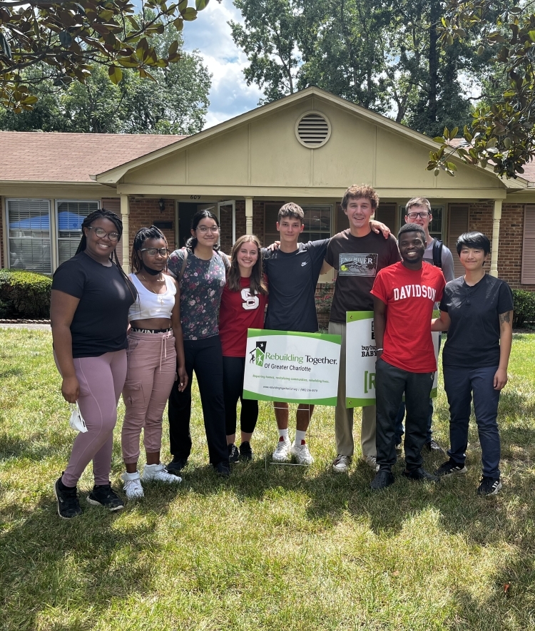 a group of students standing in front of a habitat for humanity house