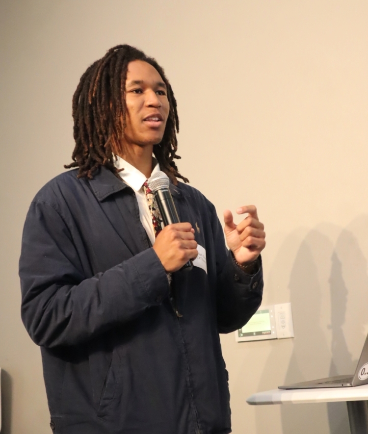 a young man speaks into a microphone at a presentation