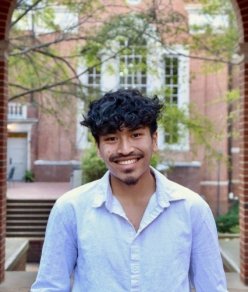 a young man with black hair and facial hair wearing a white button-up