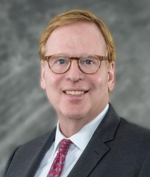 a middle aged white man with red hair wearing a suit and tie and glasses