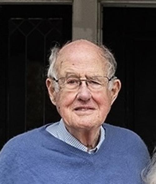 an old white man wearing glasses and collared shirt with sweater
