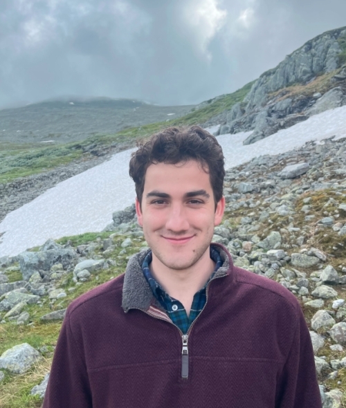 a young white man with curly dark hair wearing a red half-zip sweater