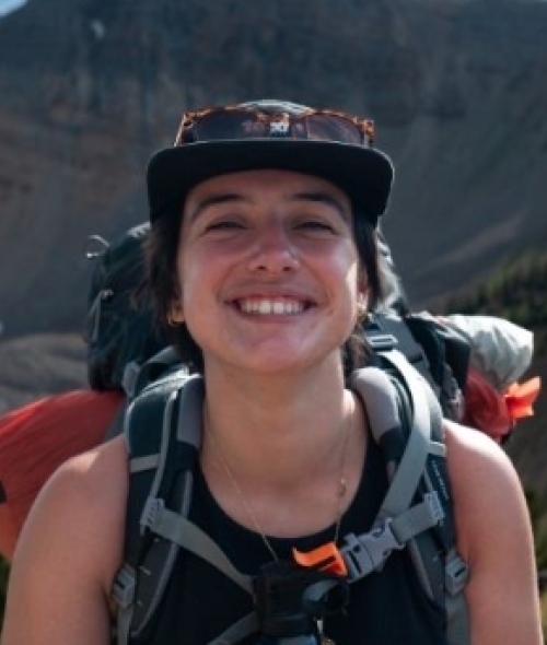 a young person hiking wearing a hat and a backpack in front of a mountain