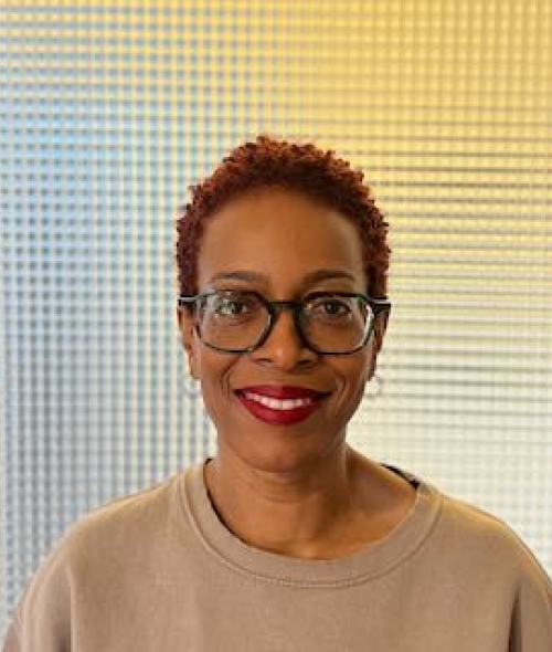 a middle aged Black woman with brown shirt in front of a yellow background