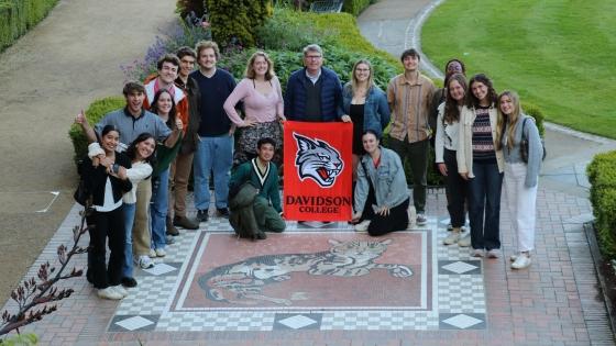 a group of students and some older people at an old castle holding a "Davidson College" banner