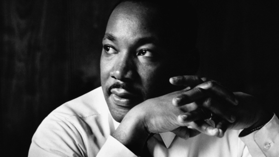 a black and white photo of a Black man wearing a white collar and holding his hands