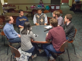 Professor and six students sit around a round table in the Union discussing economics