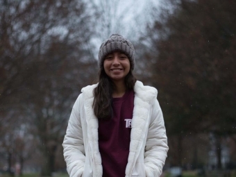 Yara poses in winter clothing in front of trees