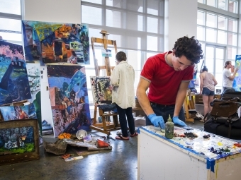 Student mixes paint in foreground while other students paint canvases in background