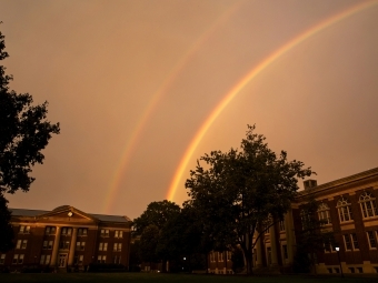 Sky rainbow over college buildings and trees 